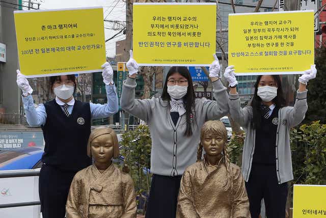 <p>High school students hold up banners to protest a recent academic paper by Harvard University professor J Mark Ramseyer, behind statues symbolising wartime sex slaves in Seoul, South Korea</p>