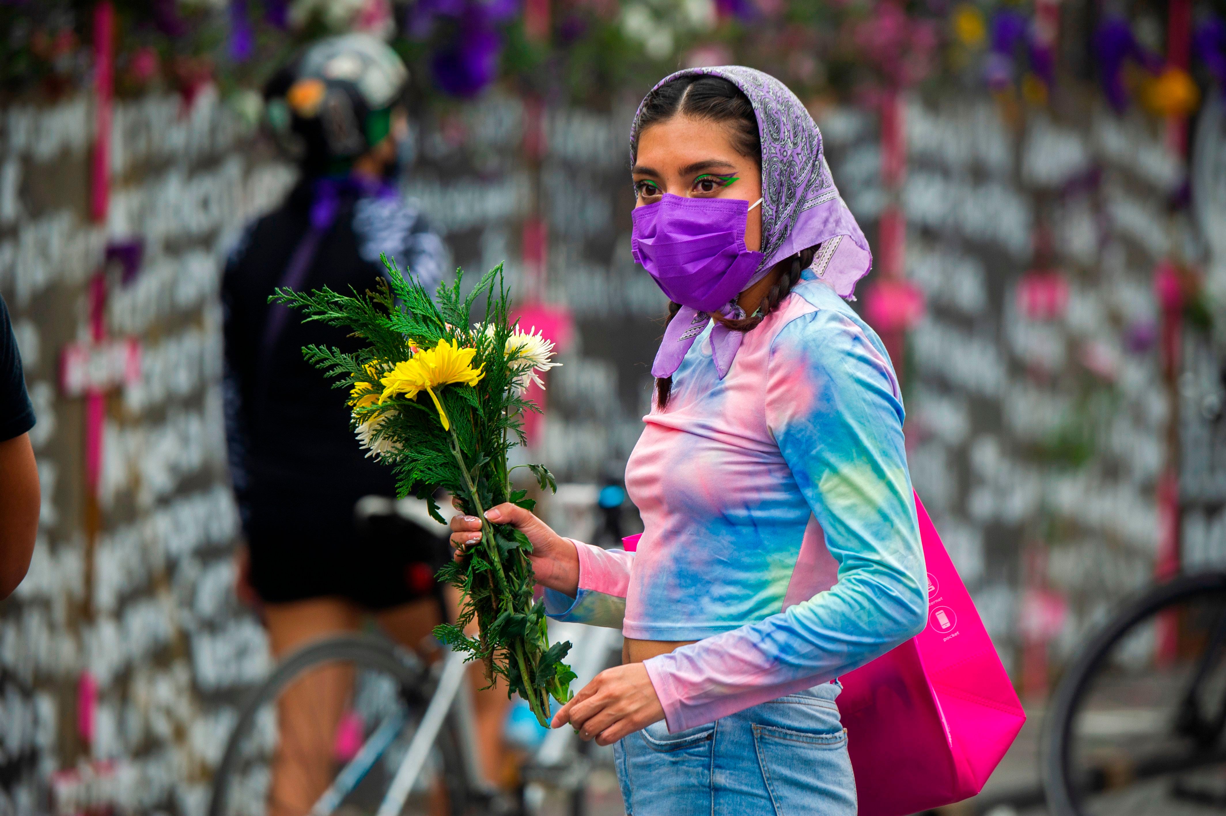 Woman by metal fence with the names of victims of femicide in Mexico City on the eve of International Women's Day