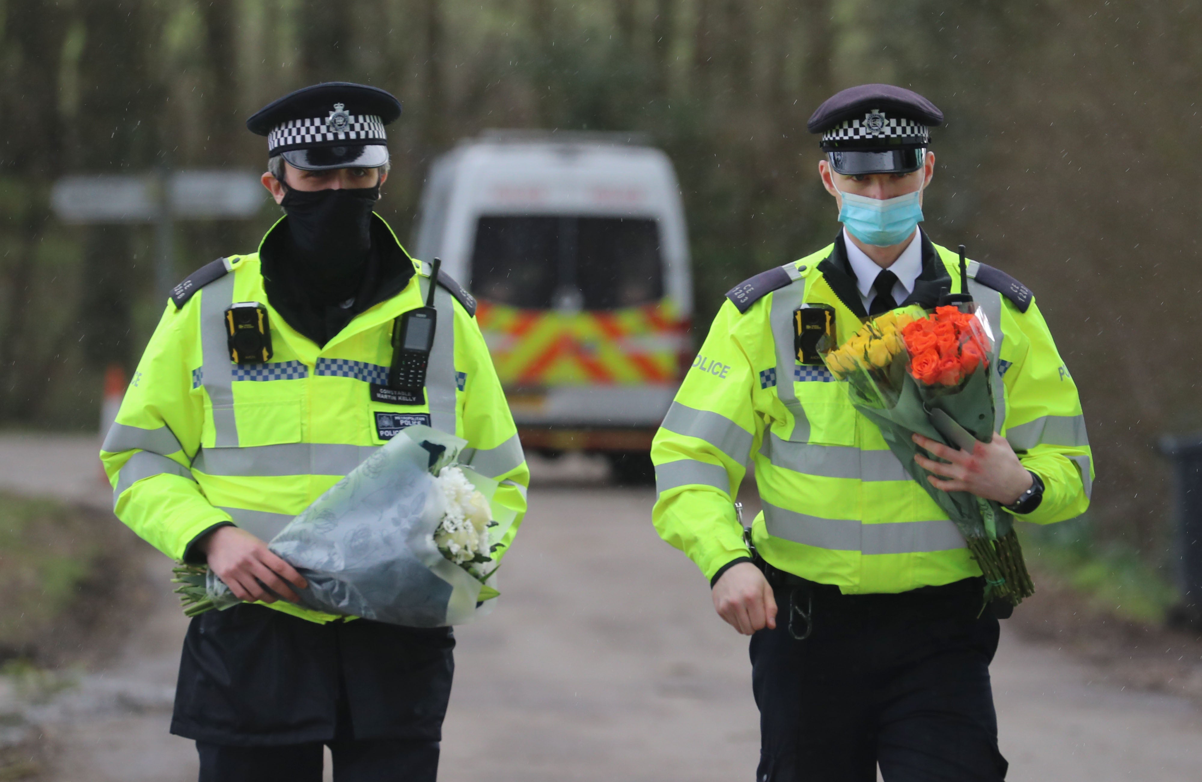 Police officers carry flowers from the public after remains were found in the search for Sarah Everard
