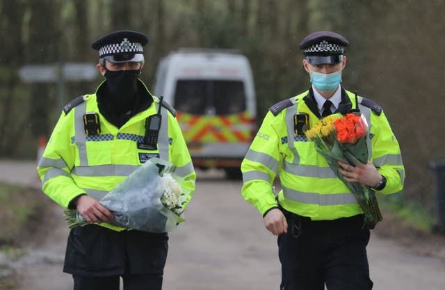 <p>Police officers carry flowers from the public after remains were found in the search for Sarah Everard</p>