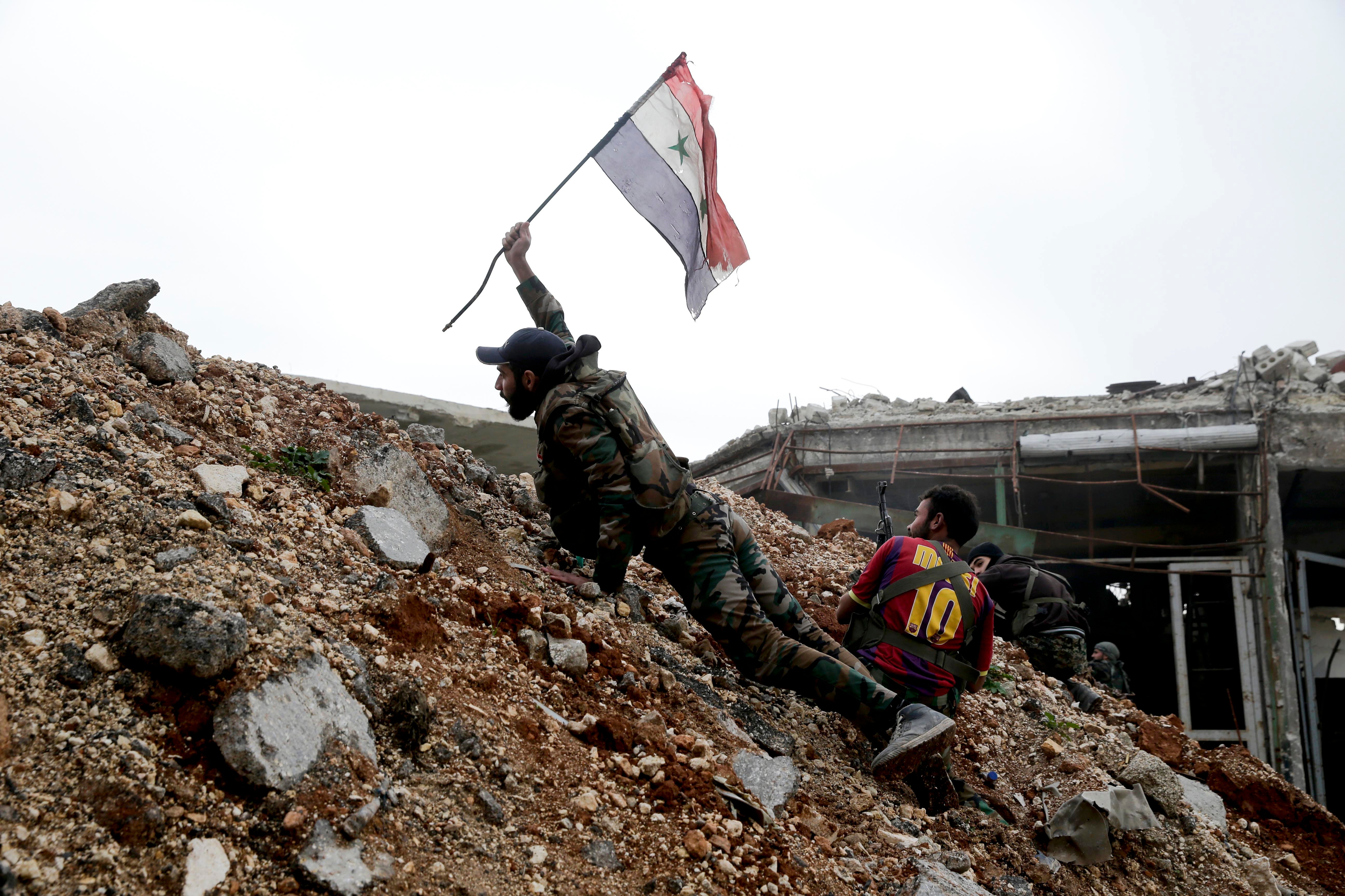 A Syrian army soldier places a Syrian national flag during a battle with rebel fighters at the Ramouseh front line, east of Aleppo in 2016