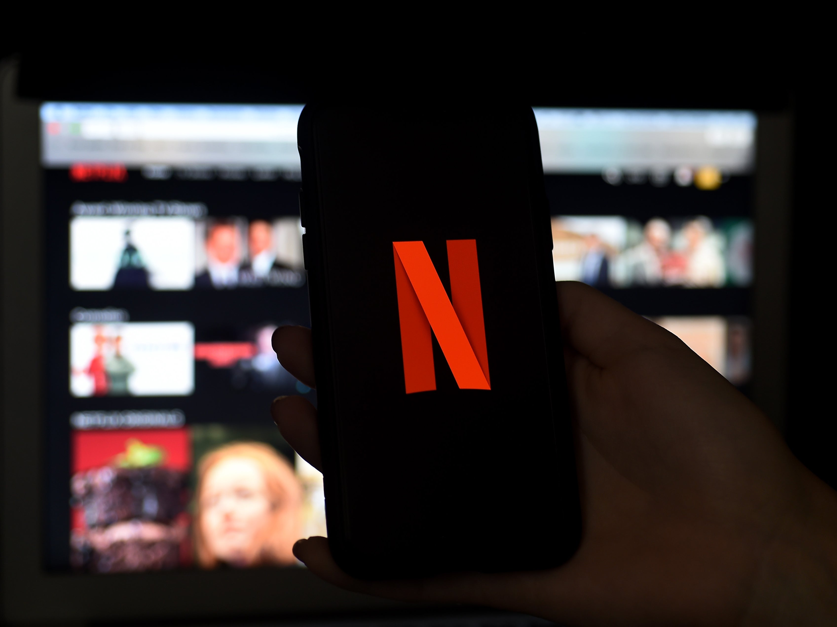 A phone is held before a TV bearing the Netflix corporate logo