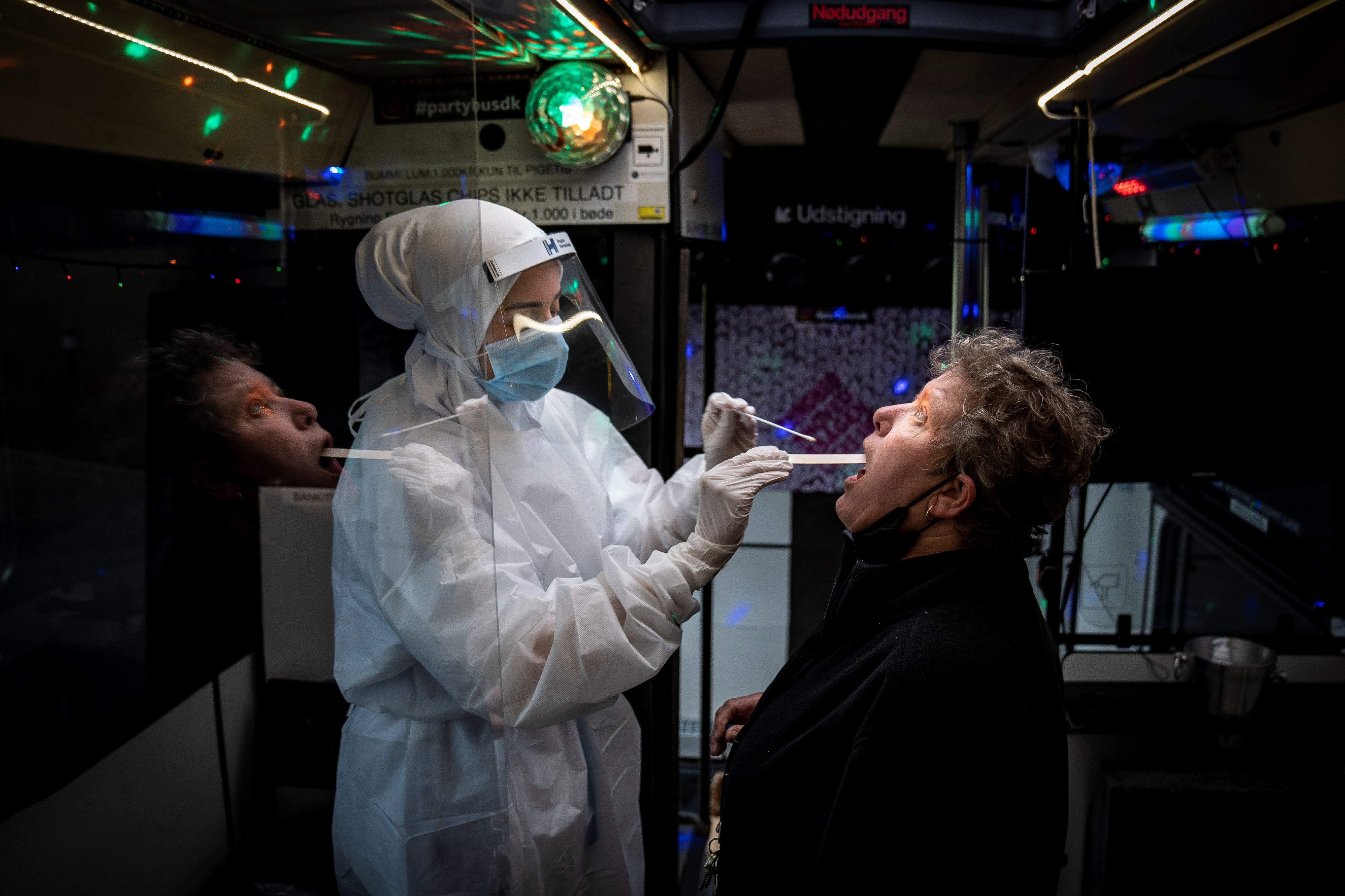 A healthcare worker takes a swab sample from a person in the Partybus, where people can listen to music while being tested, in Ishoej, Denmark
