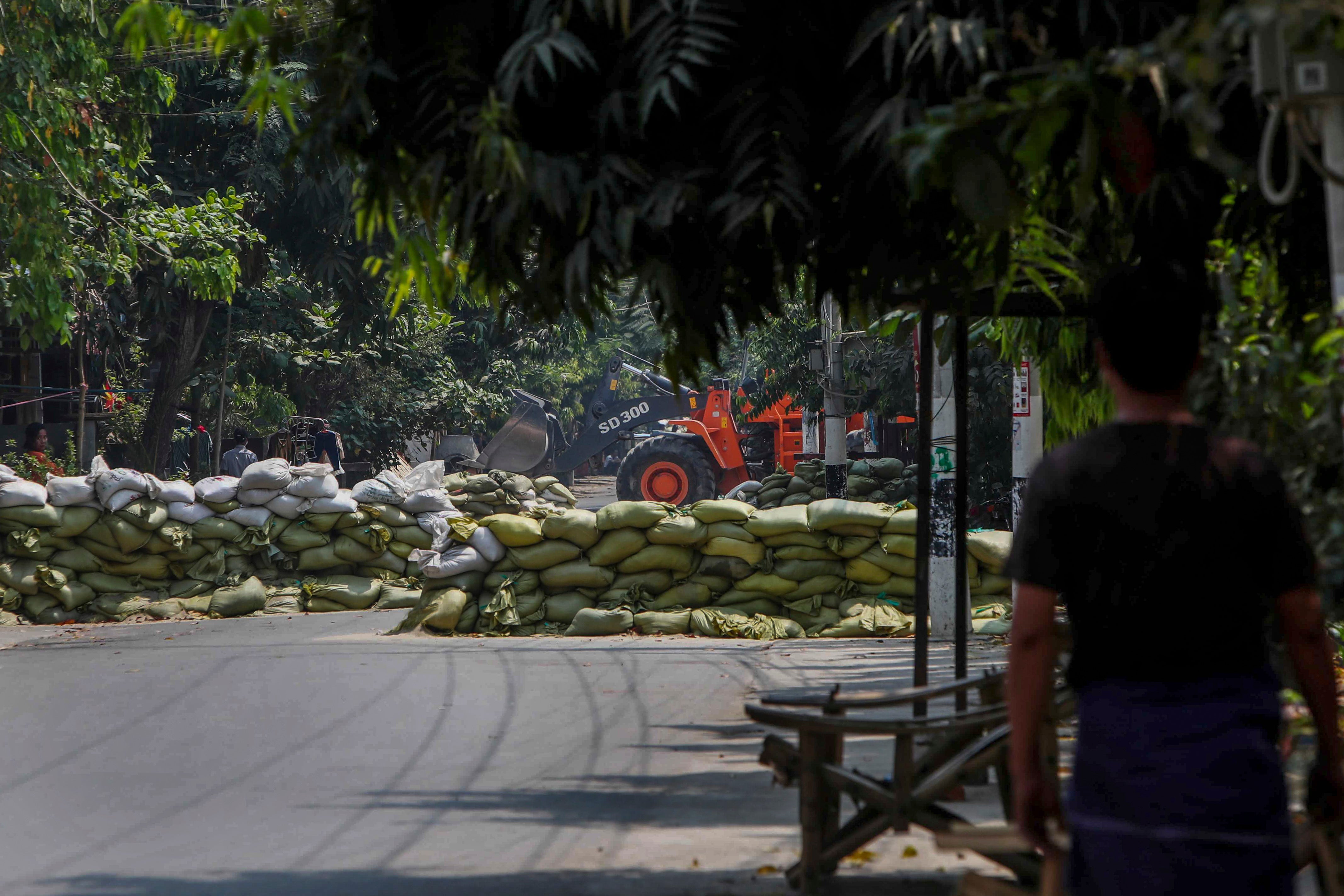 <p>A man watches as soldiers use a bulldozer to remove sandbag barricades put in place by anti-coup protesters in Mandalay, Myanmar</p>