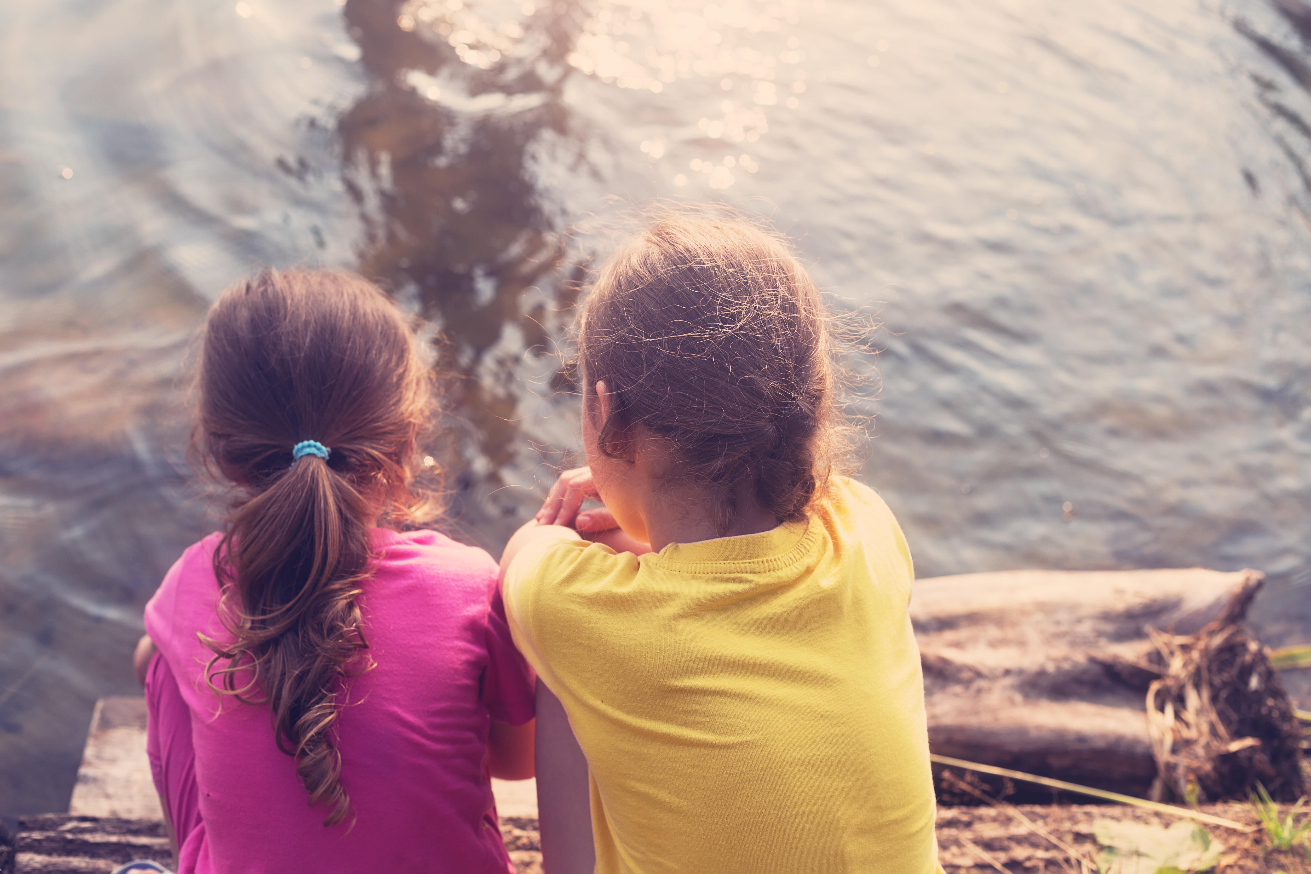 little girls sitting turn back and looking at the sea at sunset