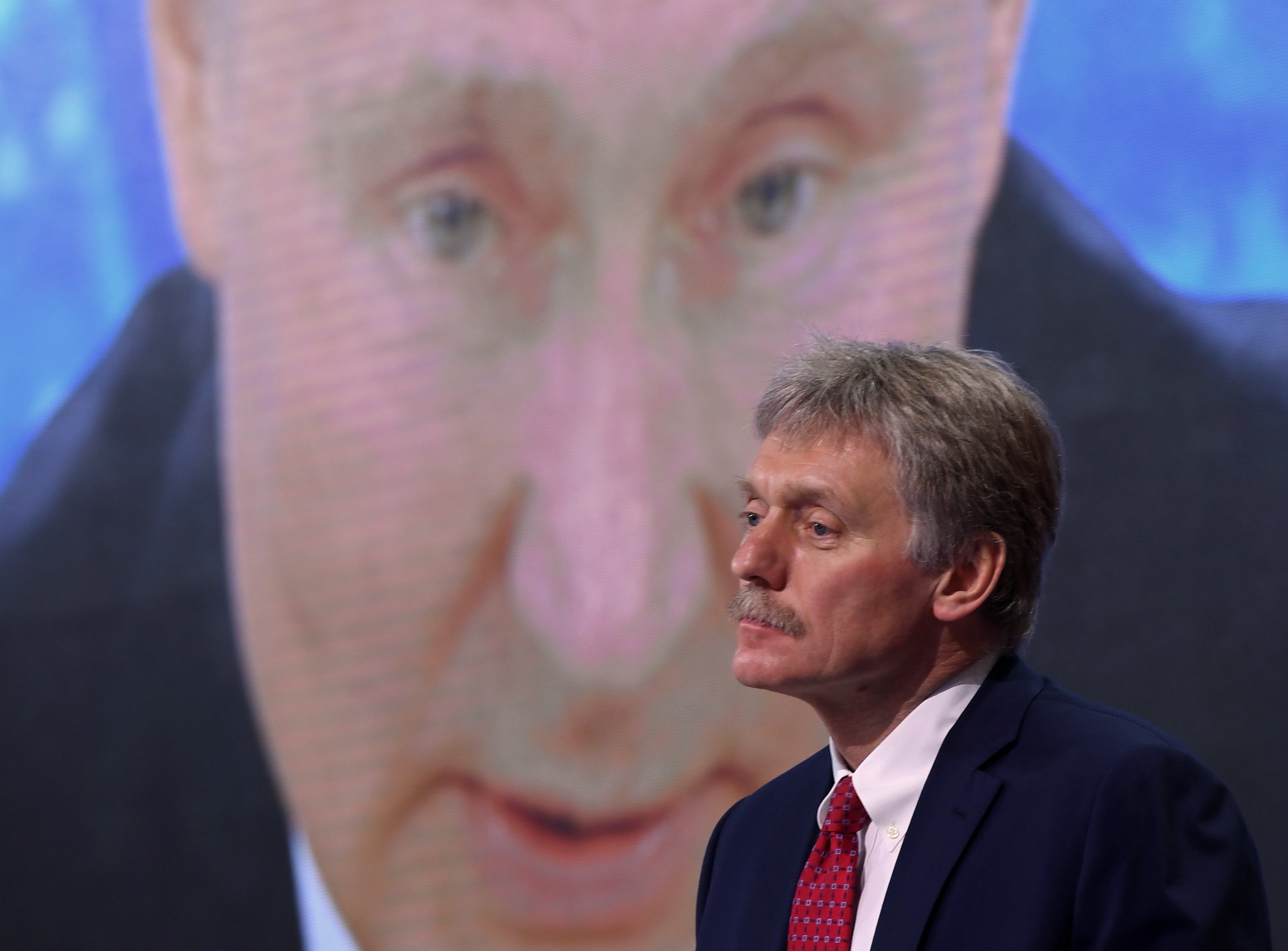 Kremlin spokesman Dmitry Peskov sits in front of a screen displaying Russian President Vladimir Putin