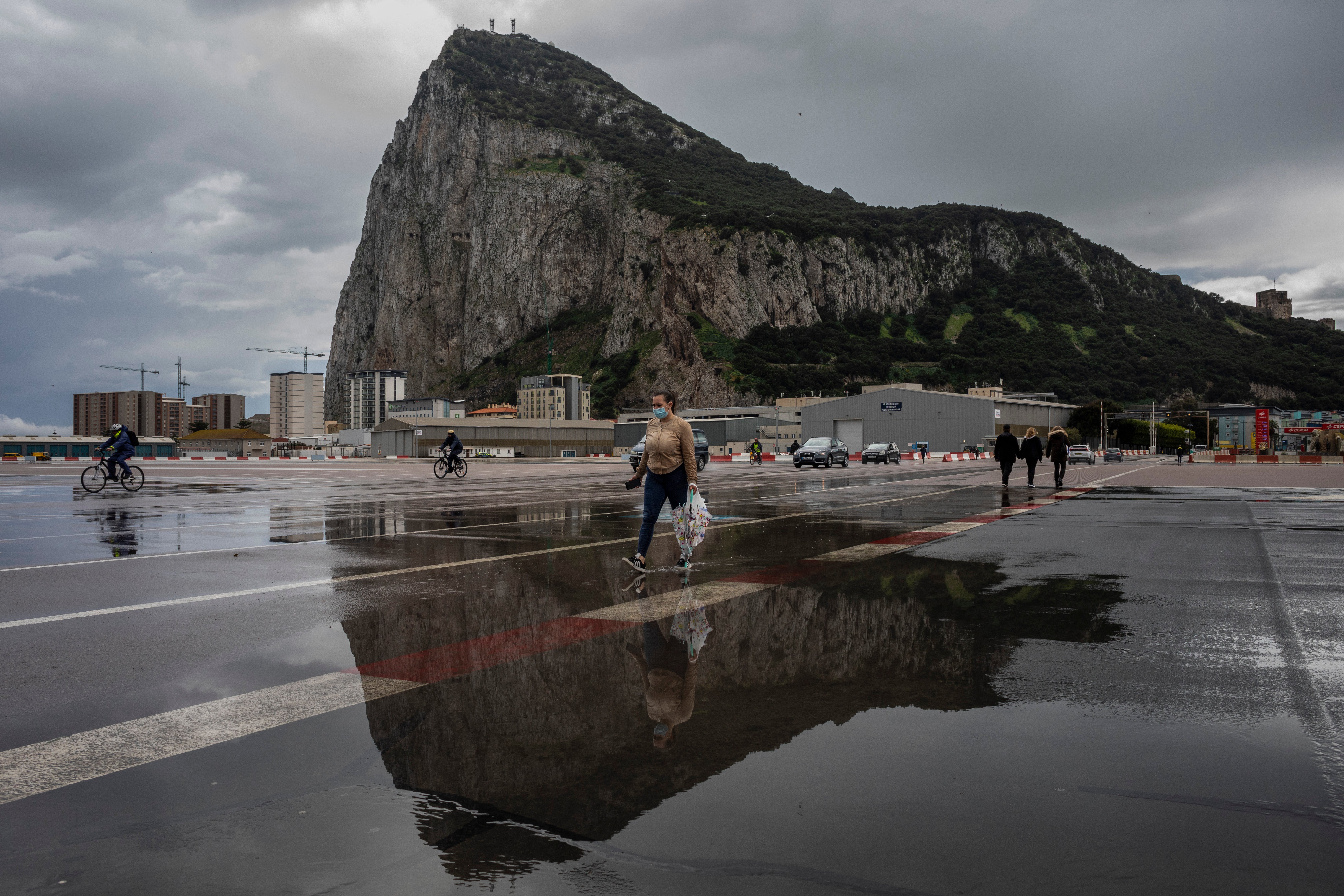 People cross the airport runway towards the border crossing with Spain, backdropped by the Rock of Gibraltar