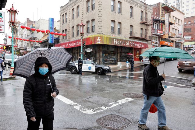 <p>Pedestrians cross the street as San Francisco Police patrol their beat in Chinatown on 18 March</p>