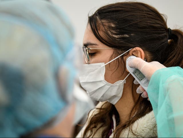 A healthcare worker uses an ear thermometer to take the temperature of a patient