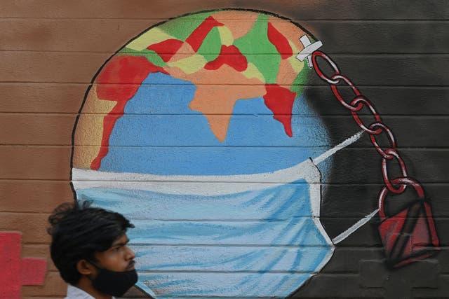 A man walks past a mural depicting the world wearing a face mask in Mumbai