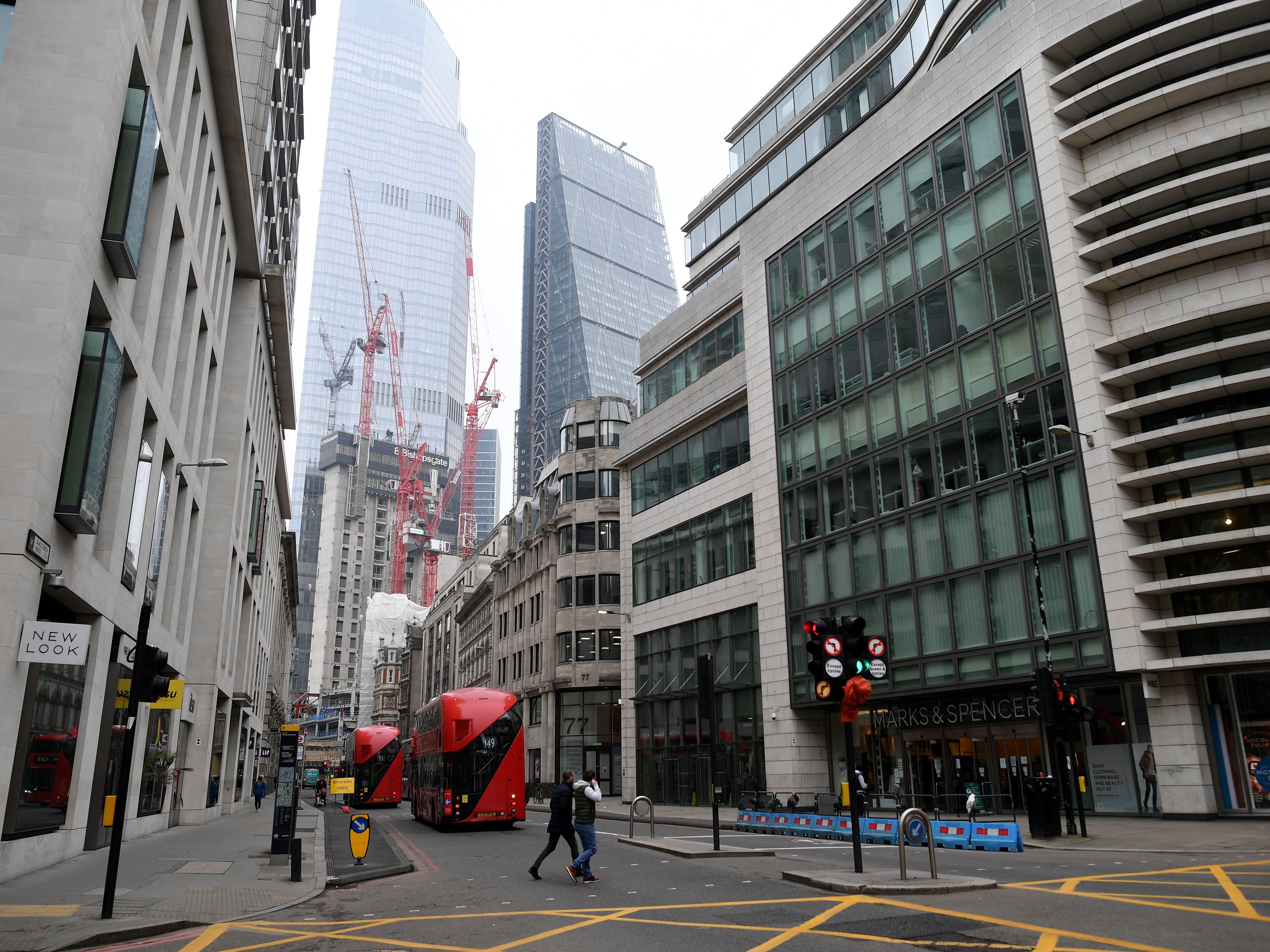 Pedestrians cross a near-deserted street in the City of London as the majority of offices remain closed