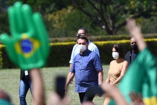 <p>Brazilian President Jair Bolsonaro and his wife Michelle walk towards supporters who gathered outside the lawns of the Alvorada Palace to celebrate his birthday, in Brasilia, on 21 March  2021</p>