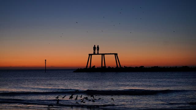 The sun rises over "The Couple" by artist Sean Henry, which sits off the coast at Newbiggin-by-the-Sea in Northumberland