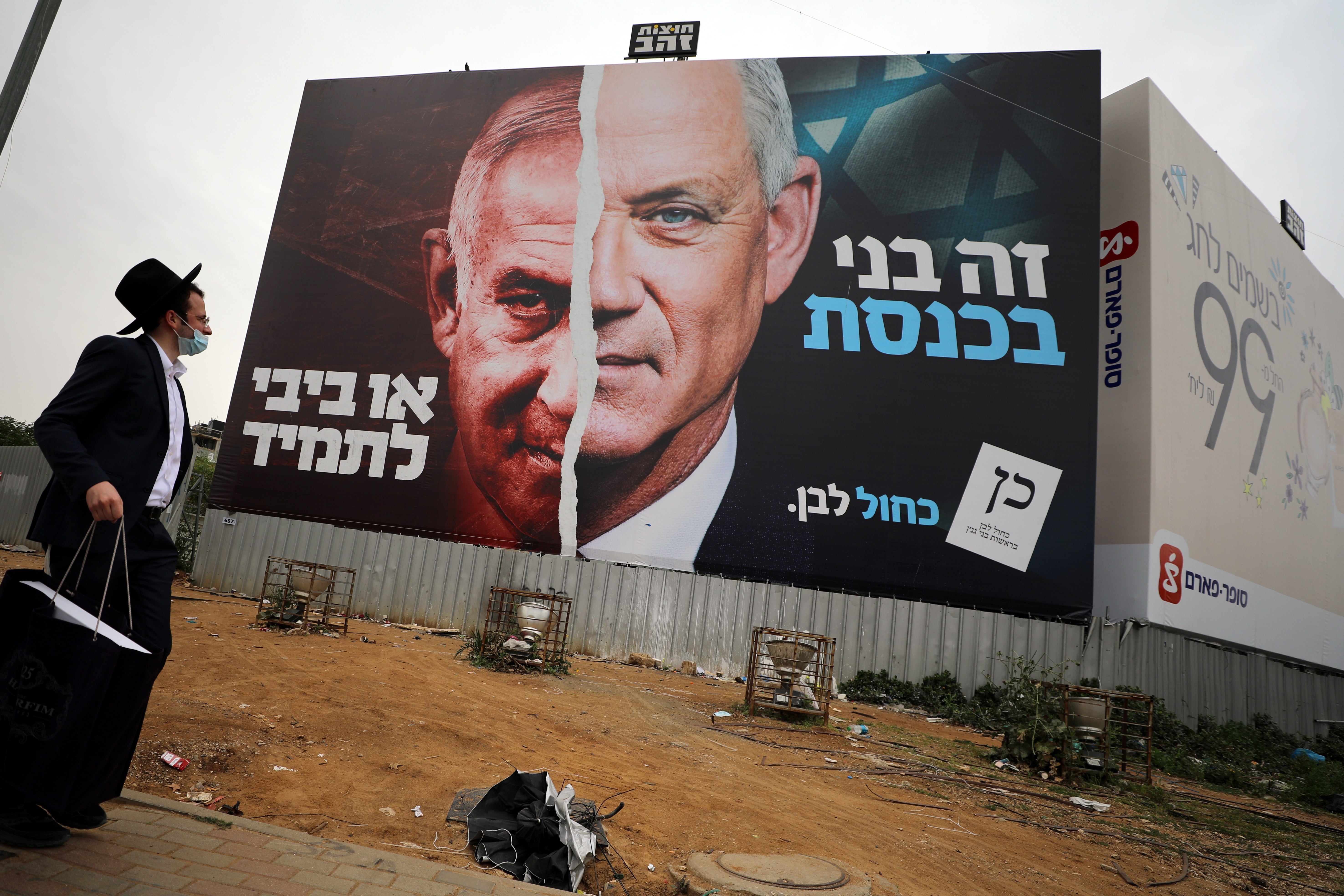 An ultra-Orthodox Jewish man looks at a Blue and White party election campaign poster depicting its leader, Israeli defence minister Benny Gantz, alongside Israeli prime minister Benjamin Netanyahu