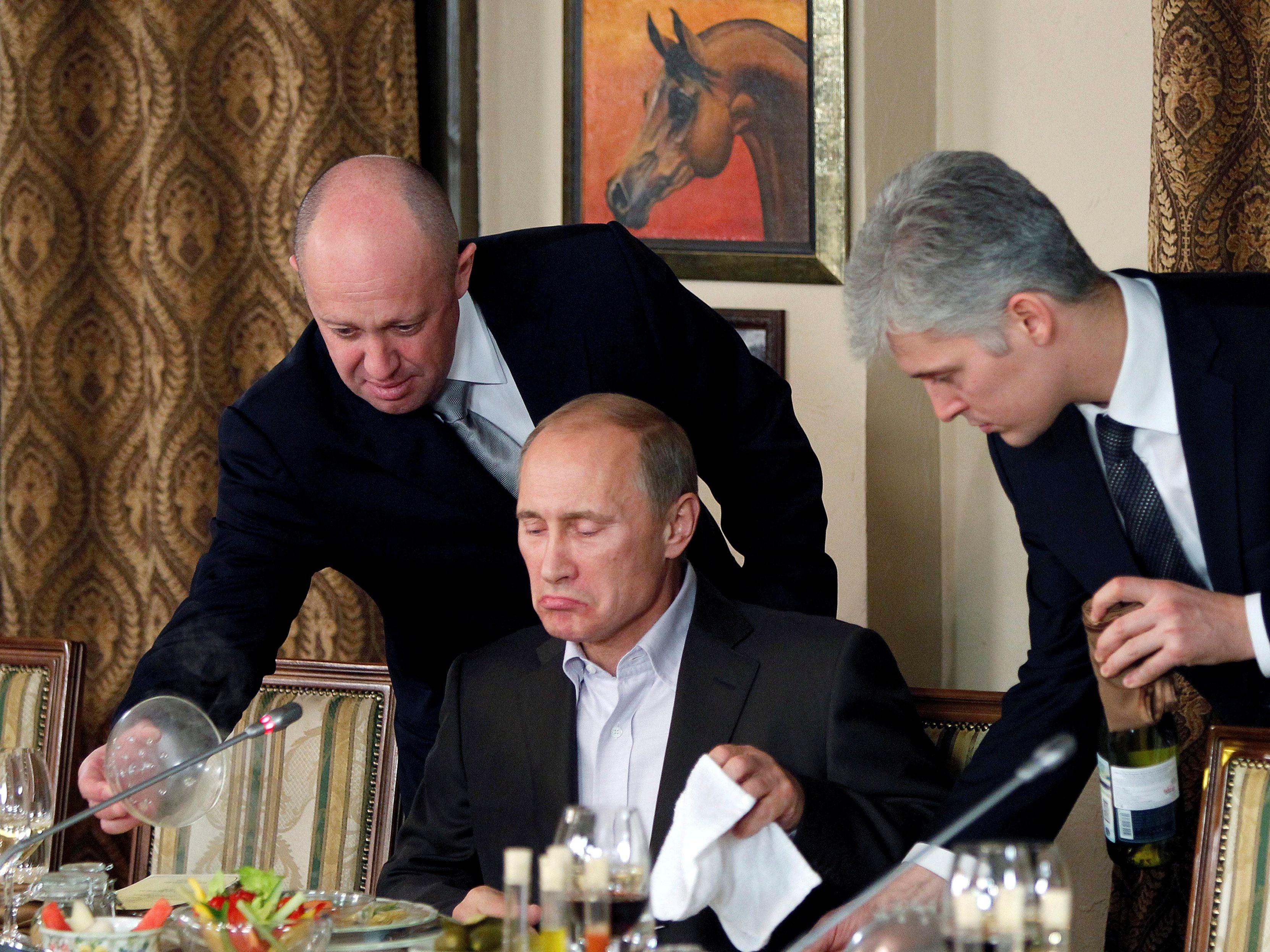 Prigozhin (L) assists Russian Prime Minister Vladimir Putin during a dinner with foreign scholars