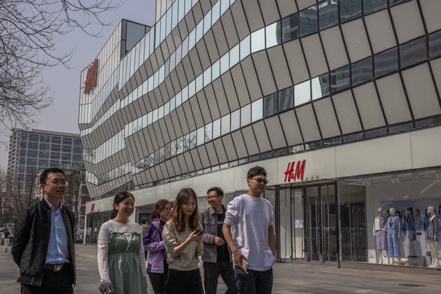 <p>People walk past an H&M store in Sanlitun, Beijing, China</p>