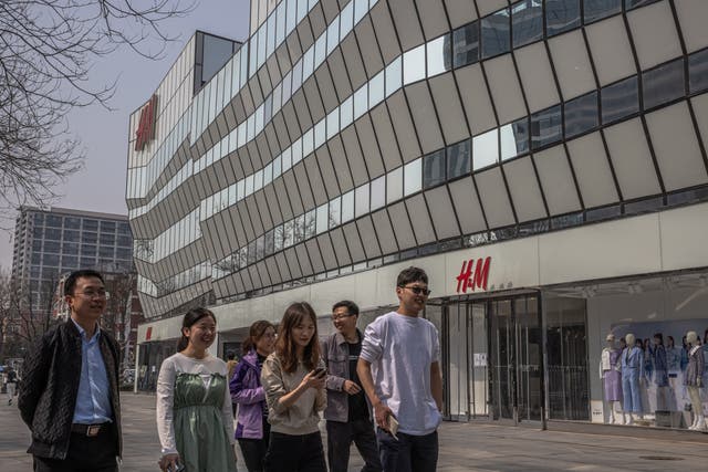<p>People walk past an H&M store in Sanlitun, Beijing, China</p>