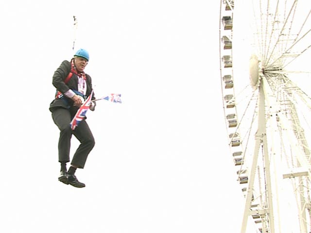 <p>Boris Johnson, the then London mayor, clutches two flags after he was left hanging in mid-air when he got stuck on a zipwire at an Olympic event at Victoria Park</p>