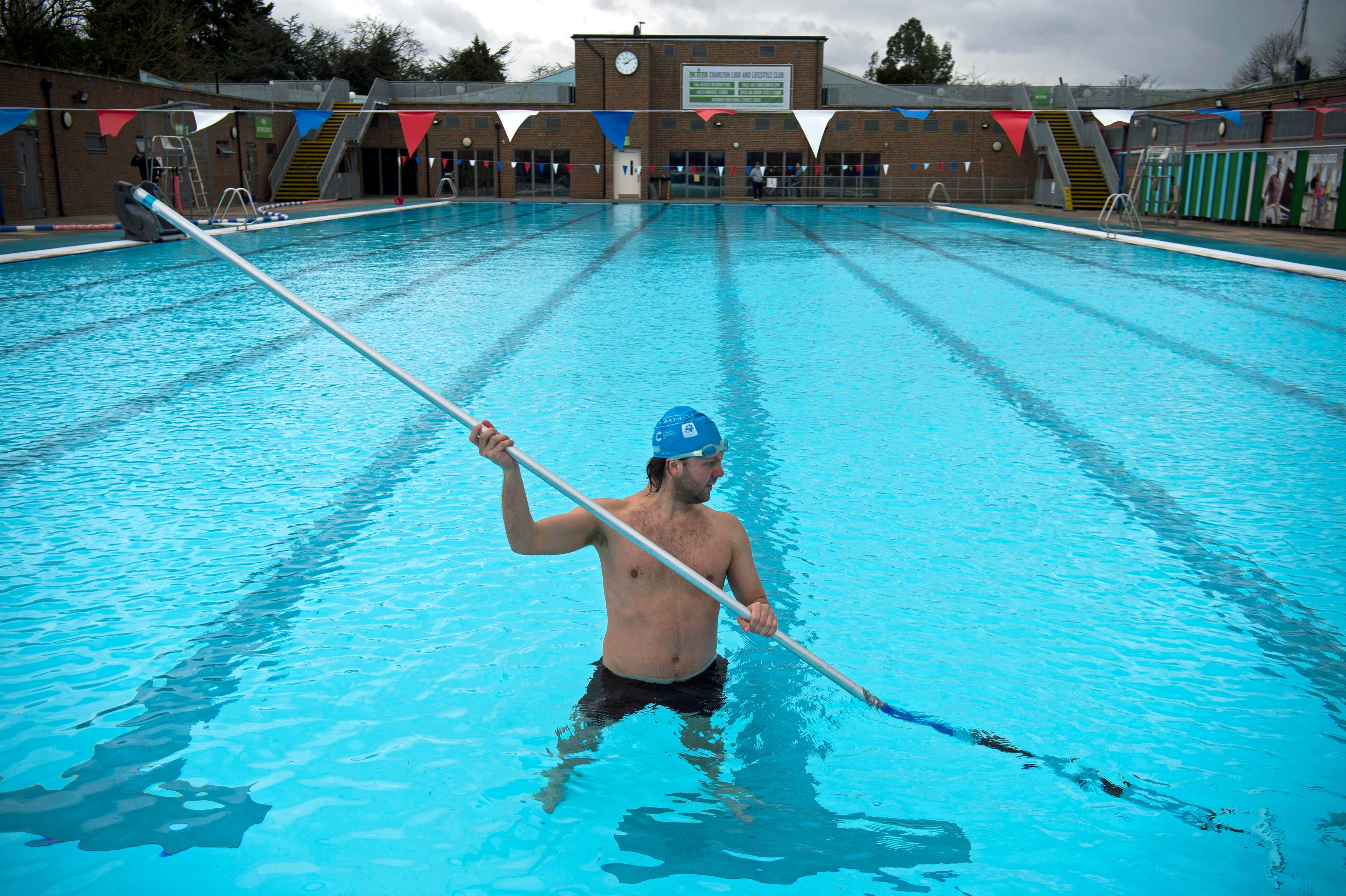 A member of staff, in the pool, cleans the bottom of the pool during pre-opening preparation and cleaning of Charlton Lido, south London, following its closure due to lockdown