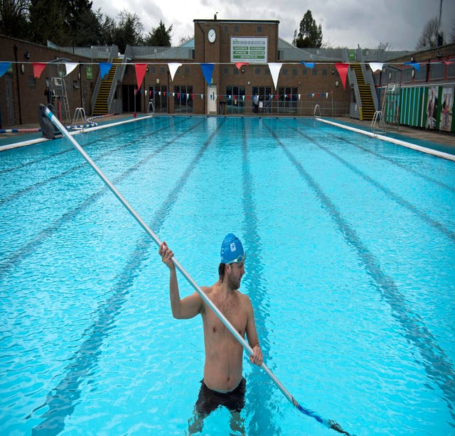 A member of staff, in the pool, cleans the bottom of the pool during pre-opening preparation and cleaning of Charlton Lido, south London, following its closure due to lockdown