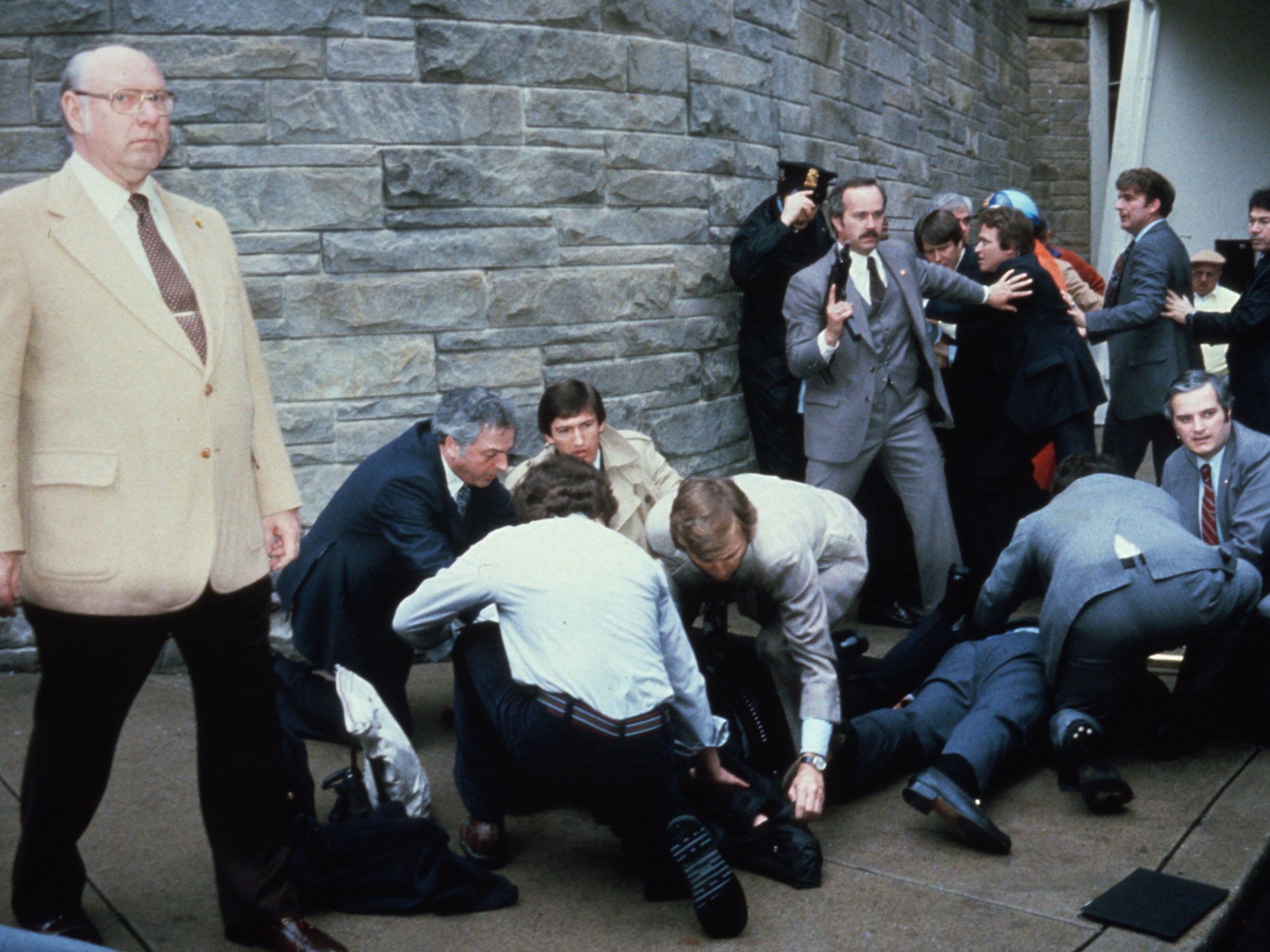 John Hinckley Jr is held down by police after attempting to kill Ronald Reagan, while shooting victims James Brady and Timothy McCarthy are tended to