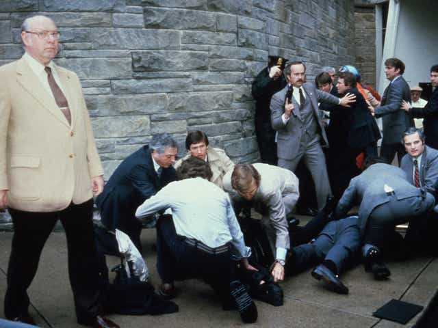 <p>John Hinckley Jr is held down by police after attempting to kill Ronald Reagan, while shooting victims James Brady and  Timothy McCarthy are tended to</p>
