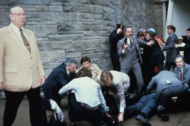 <p>John Hinckley Jr is held down by police after attempting to kill Ronald Reagan, while shooting victims James Brady and  Timothy McCarthy are tended to</p>