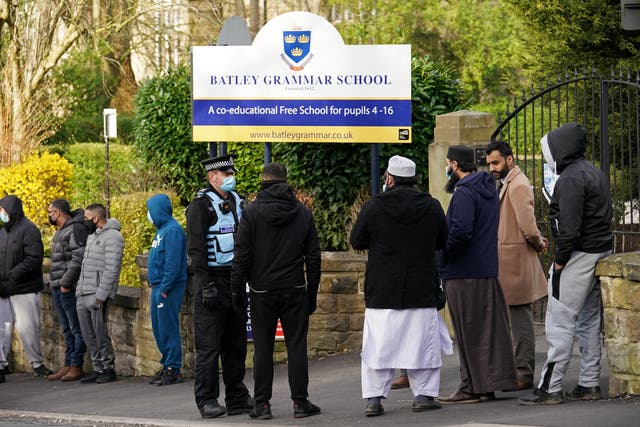 A police officer stands with protesters outside Batley Grammar School