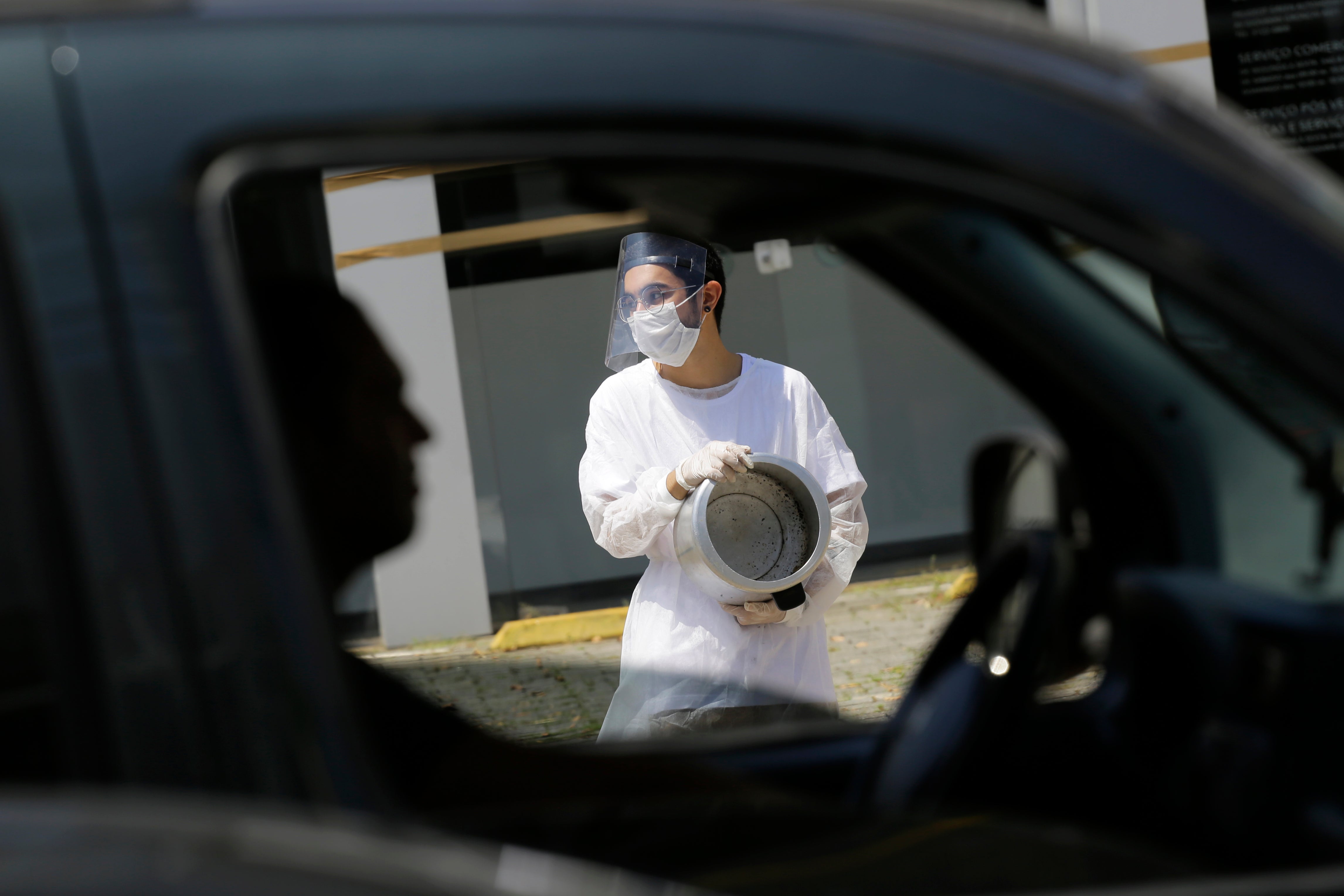 A commuter sits at a light where a protester holds an empty pot to demand food aid for those affected economically by the COVID-19 pandemic during a demonstration against the government's response to the pandemic