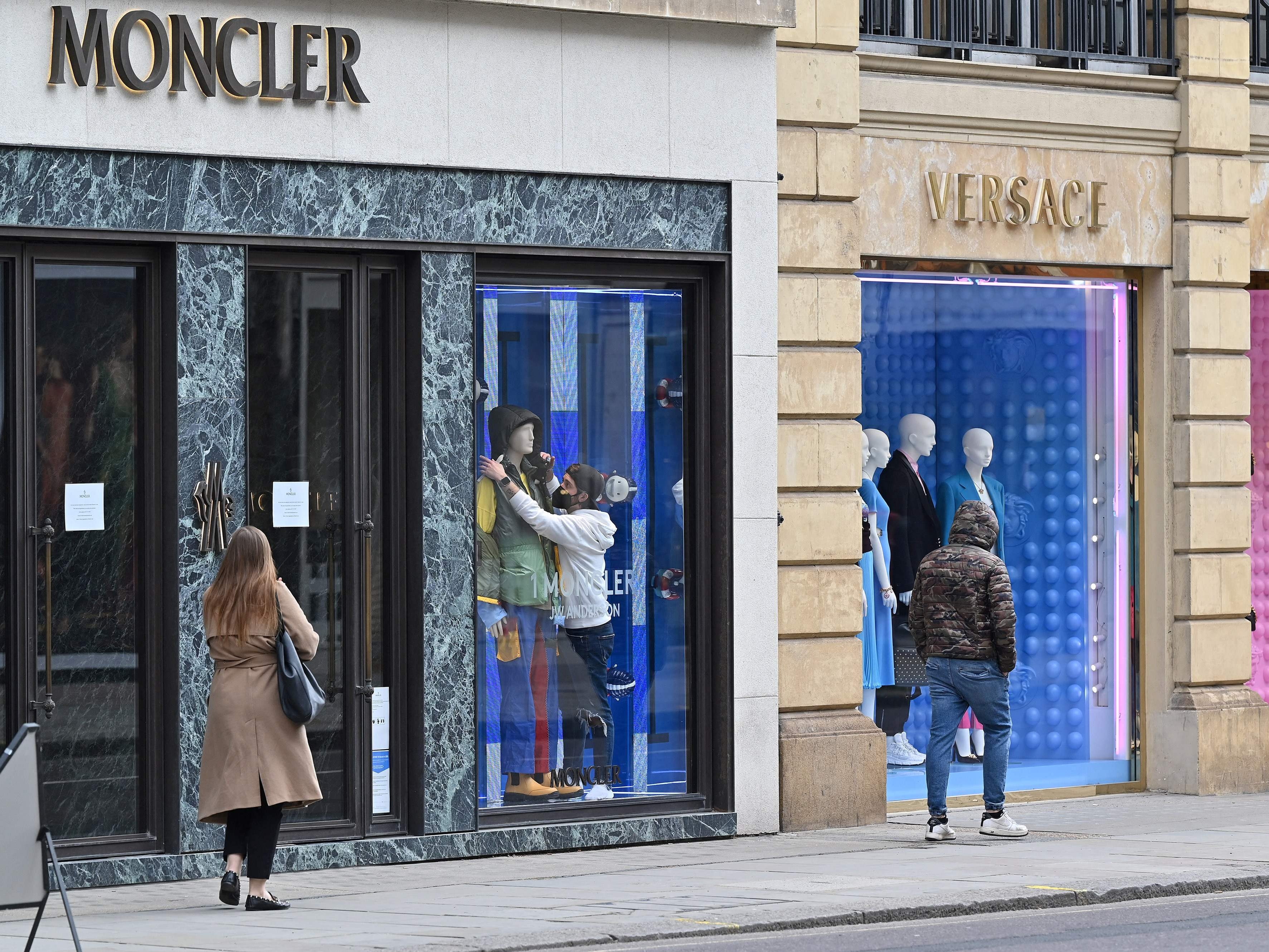 A worker organises clothes on a mannequin in the window display of a Moncler shop, closed down due to Covid-19 restrictions, in London