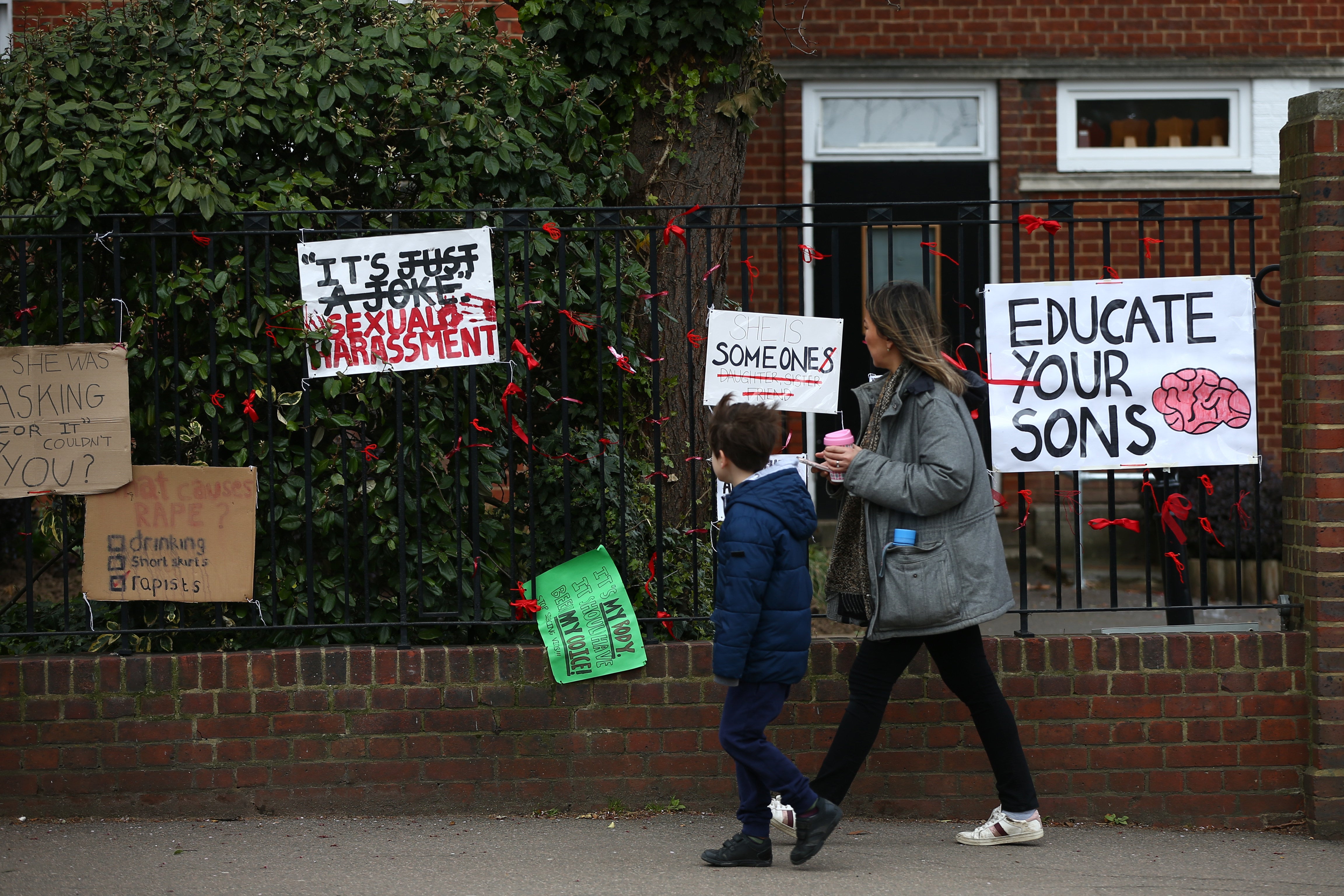 Woman and child walk past placards pinned to the fence outside James Allen's Girls' School (JAGS)