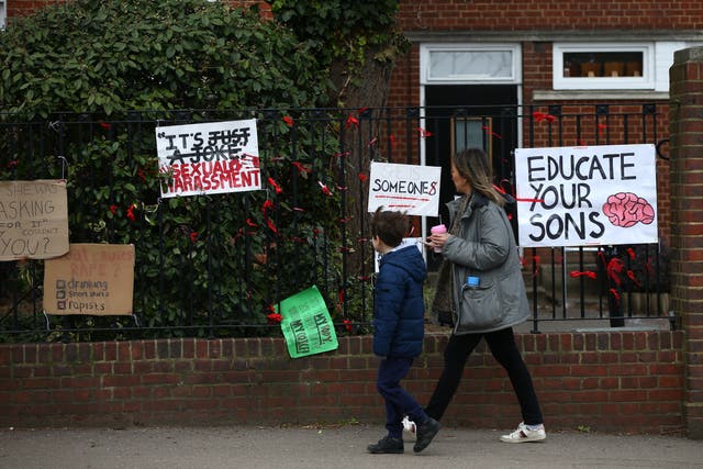 <p>Woman and child walk past placards pinned to the fence outside James Allen's Girls' School (JAGS)</p>