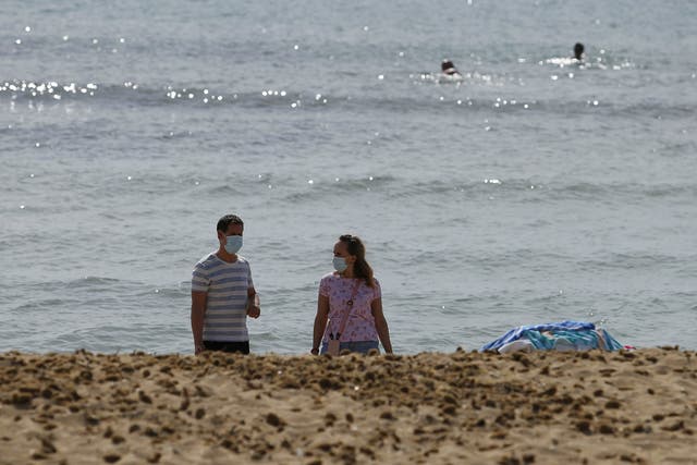People wearing face masks walk next to the sea at Playa de Palma beach in Palma de Mallorca