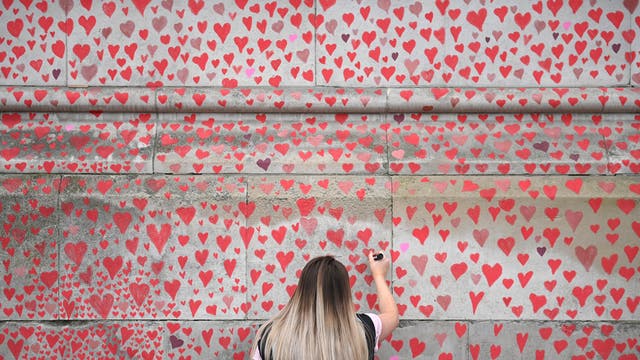 A woman adds a heart to the National Covid Memorial Wall in London