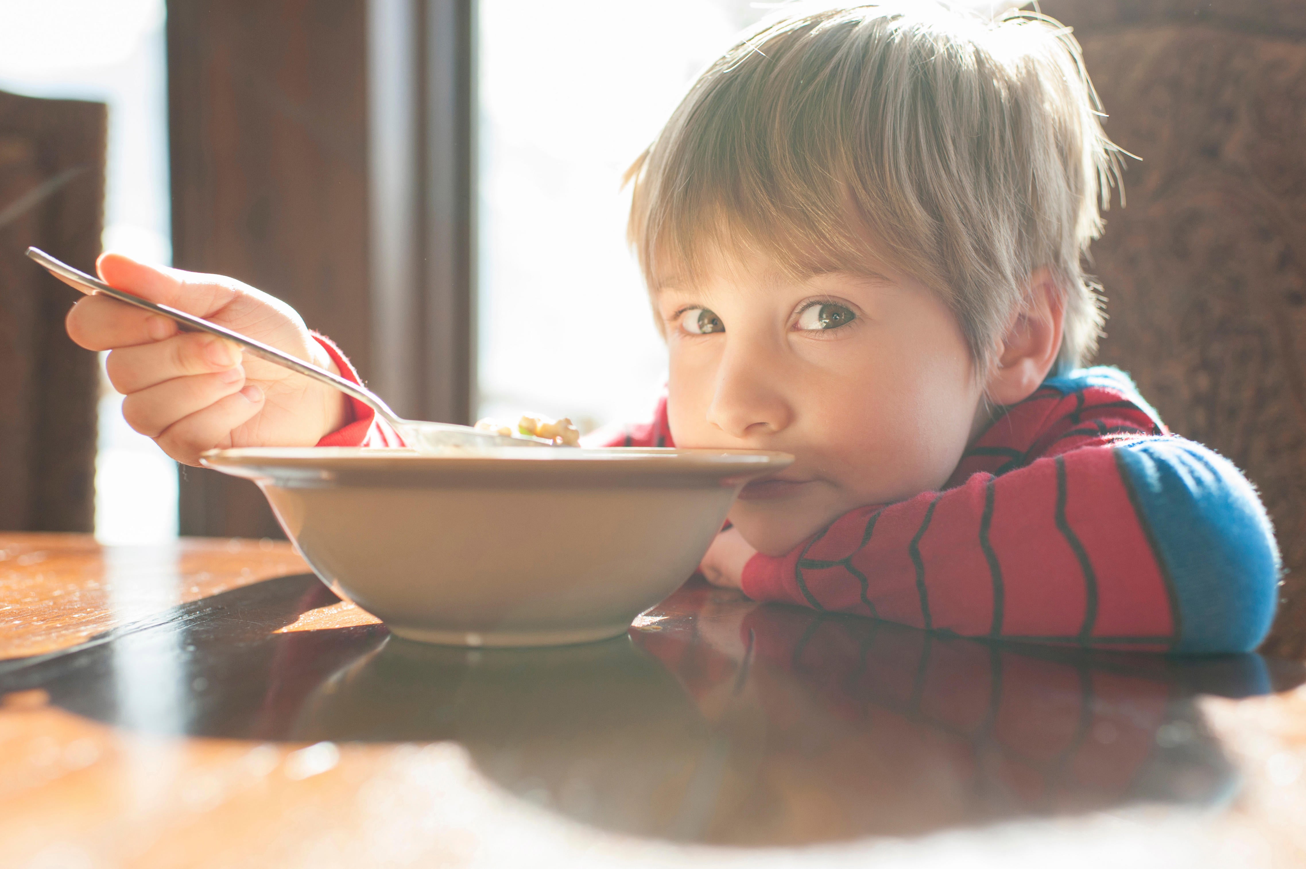 Portrait of boy eating food while leaning on table at home