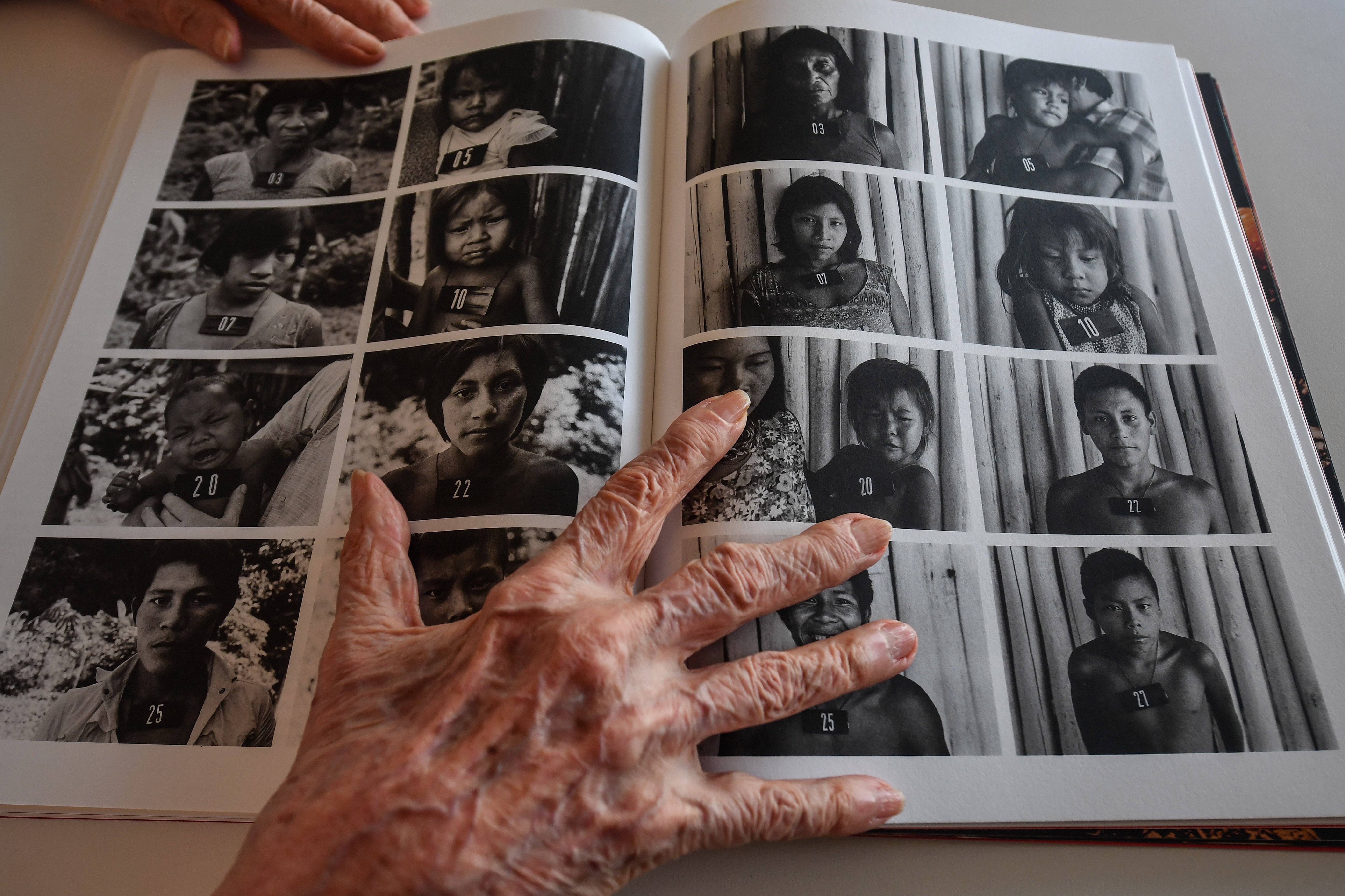 Claudia Andujar keeps a book open on a page with portraits of indigenous people