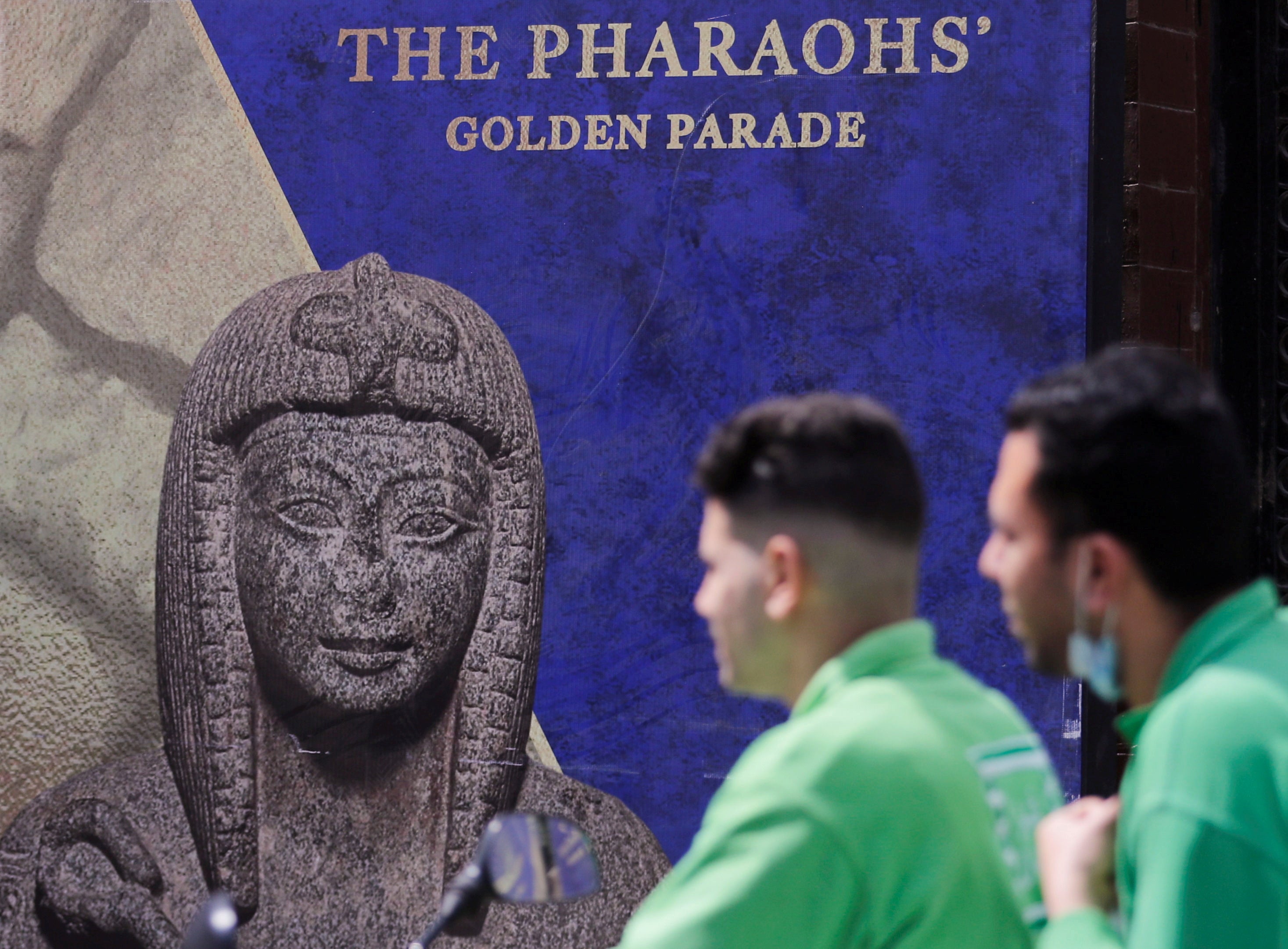 Men pass in front of poster for the Pharaohs’ Golden Parade after the renovation of Tahrir Square for transferring 22 mummies