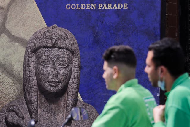 <p>Men pass in front of poster for the Pharaohs’ Golden Parade after the renovation of Tahrir Square for transferring 22 mummies </p>