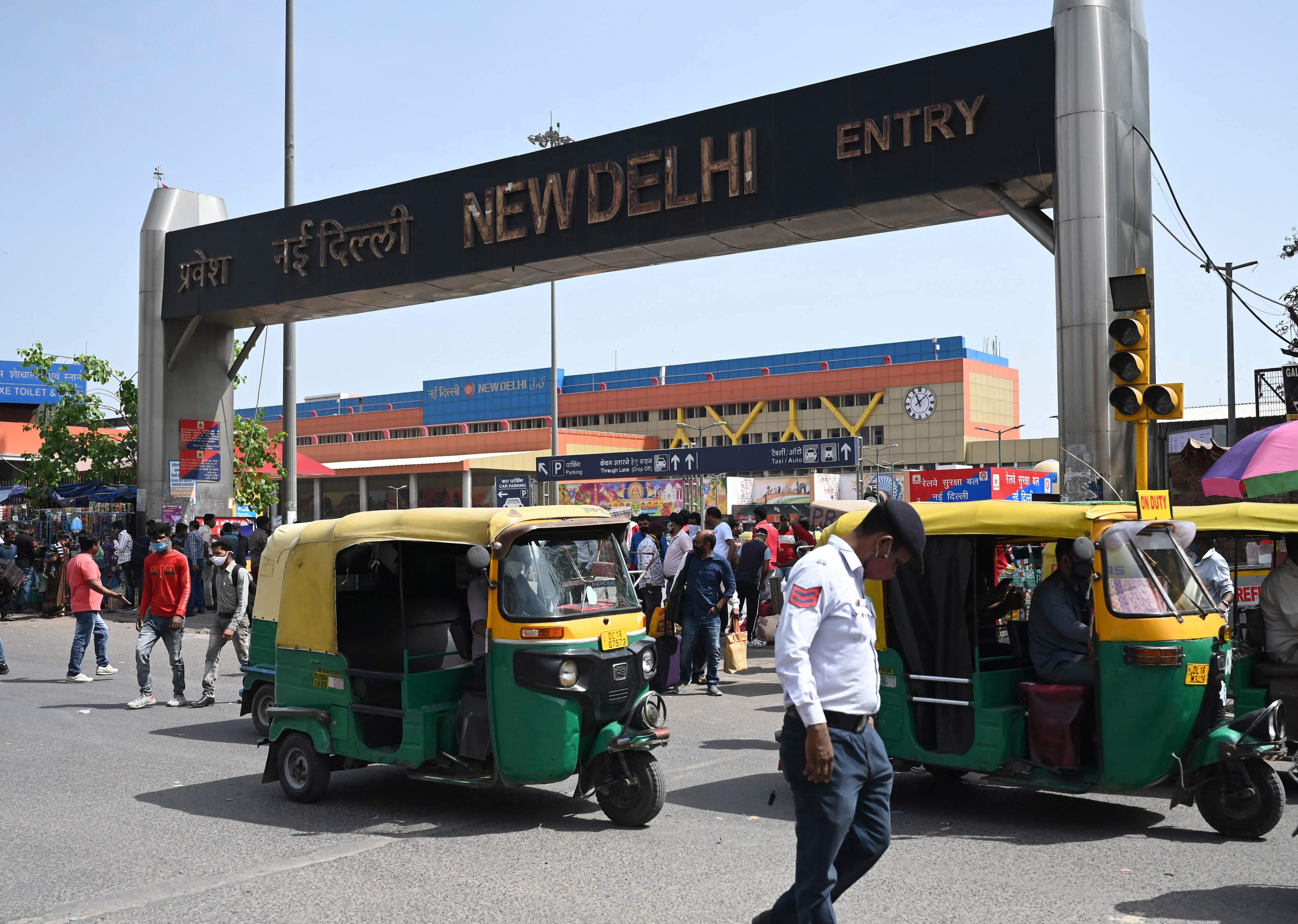 A traffic policeman, people and vehicles make their way near an entrance of the New Delhi Railway