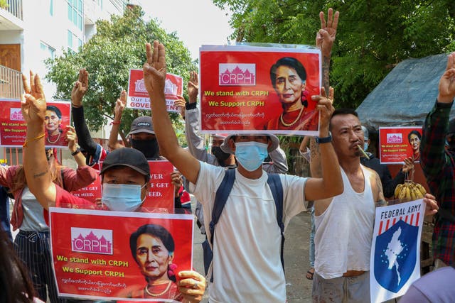 <p>Anti-coup protesters flash the three-fingered symbol of resistance while holding slogans bearing pictures of deposed leader Aung San Suu Kyi during a demonstration in Yangon, Myanmar on Wednesday 7 April</p>