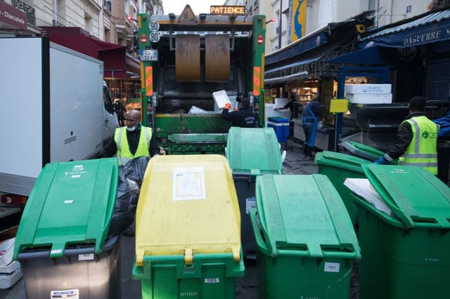 Rubbish collectors of the Paris municipality cleaning service "Proprete de Paris", wearing face masks, collect waste bins to be emptied in a garbage truck in Paris