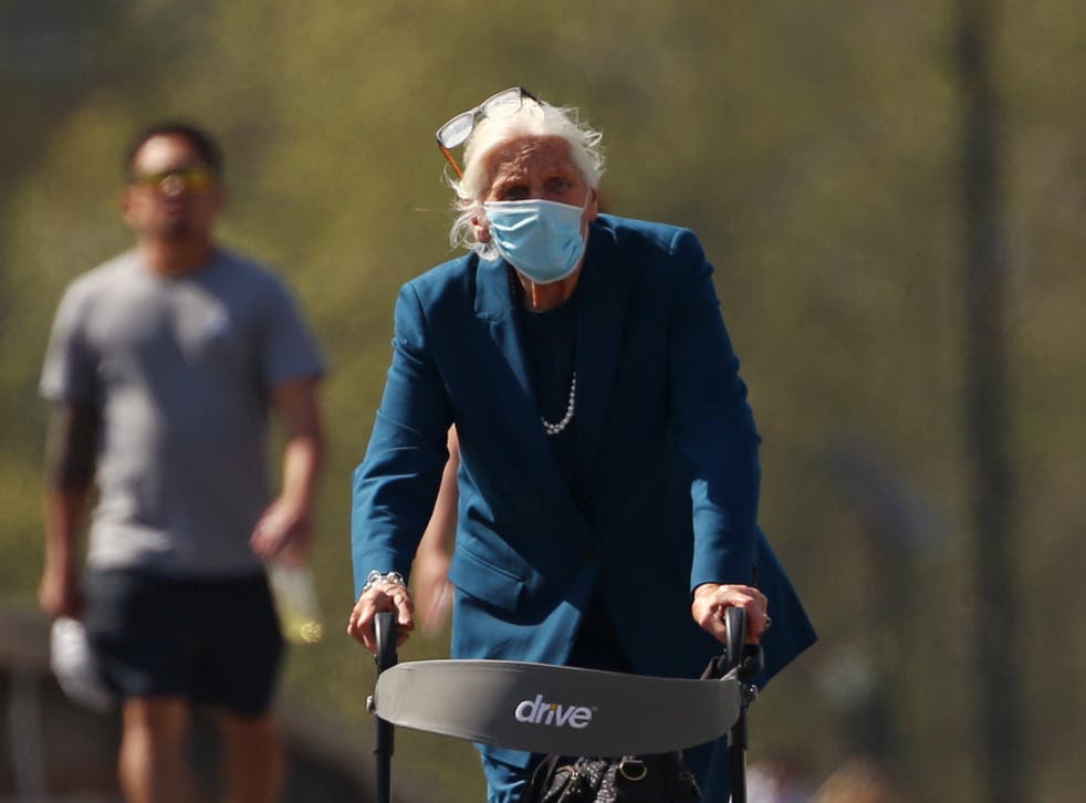 An elderly woman wearing a face mask and using a walker on Westminster Bridge, London