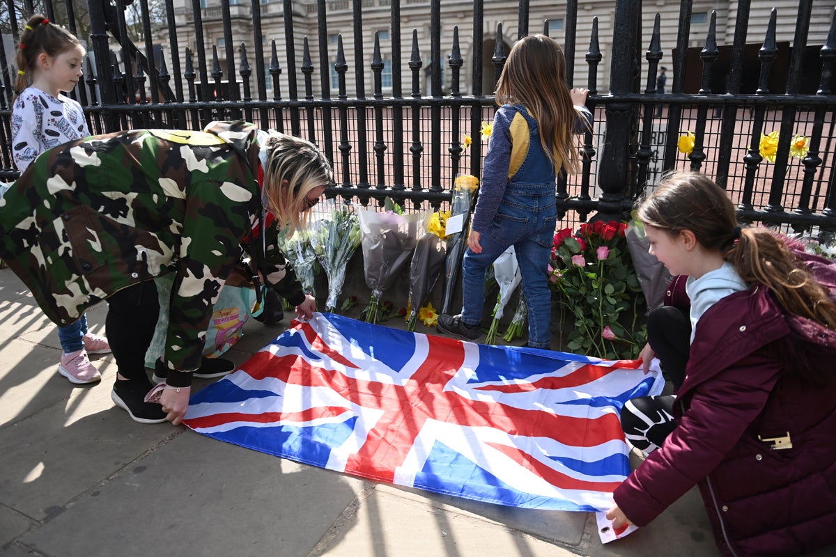 People place a Union Jack flag next to flowers and condolence messages outside Buckingham Palace