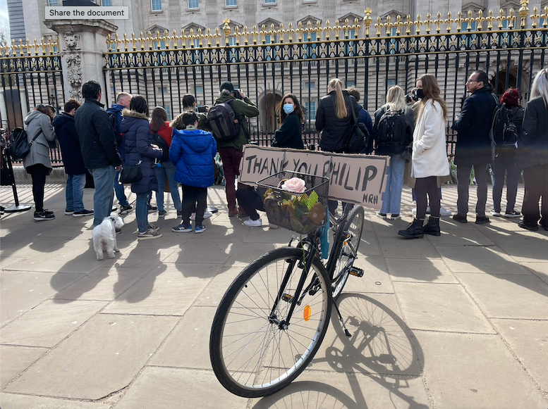 A bicycle with a sign saying ‘Thank you Philip HRH’ and flowers in its basket is parked outside Buckingham Palace