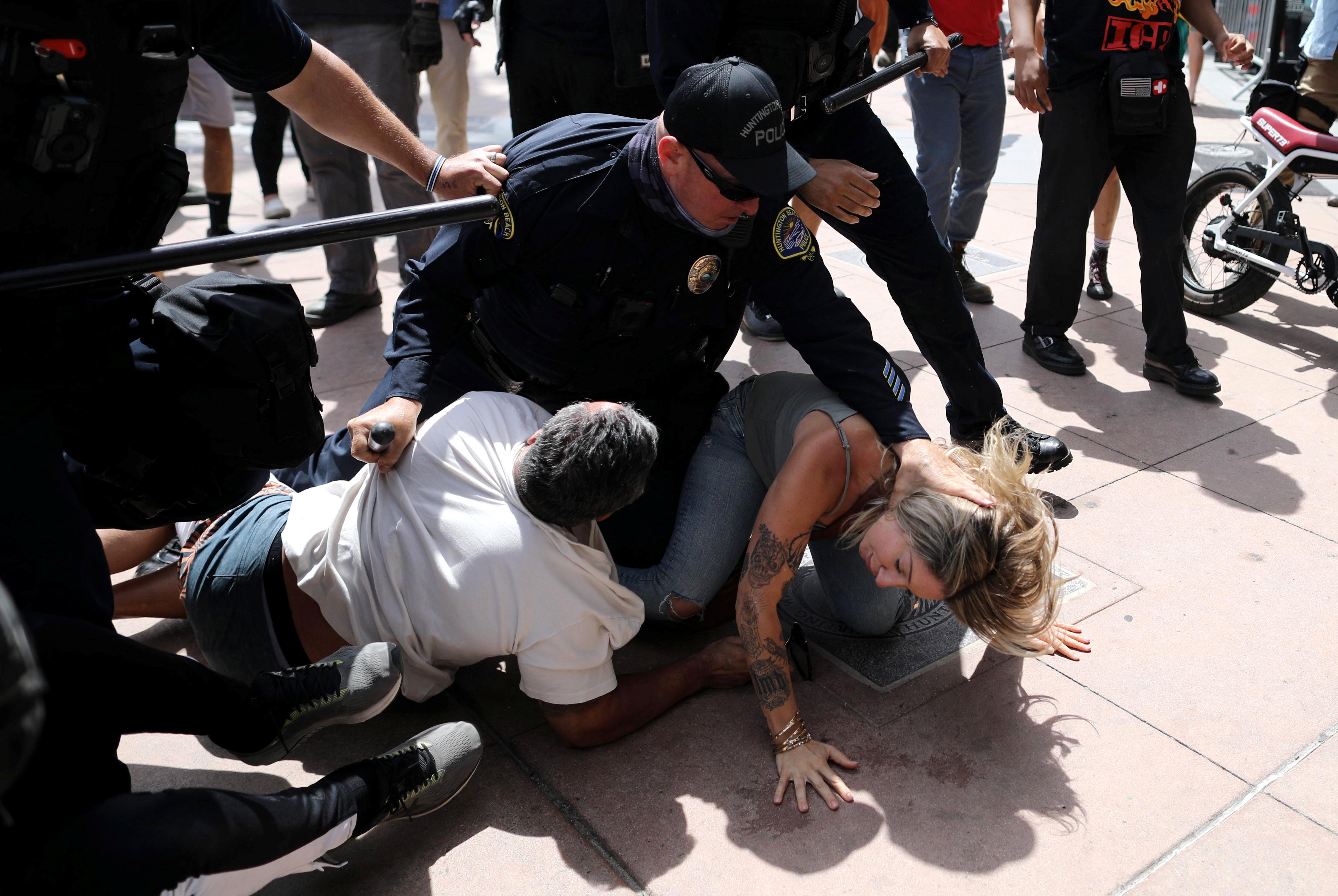 A police officer pins a woman down during confrontations with protesters in Huntington Beach