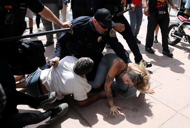 <p>A police officer pins a woman down during confrontations with protesters in Huntington Beach</p>