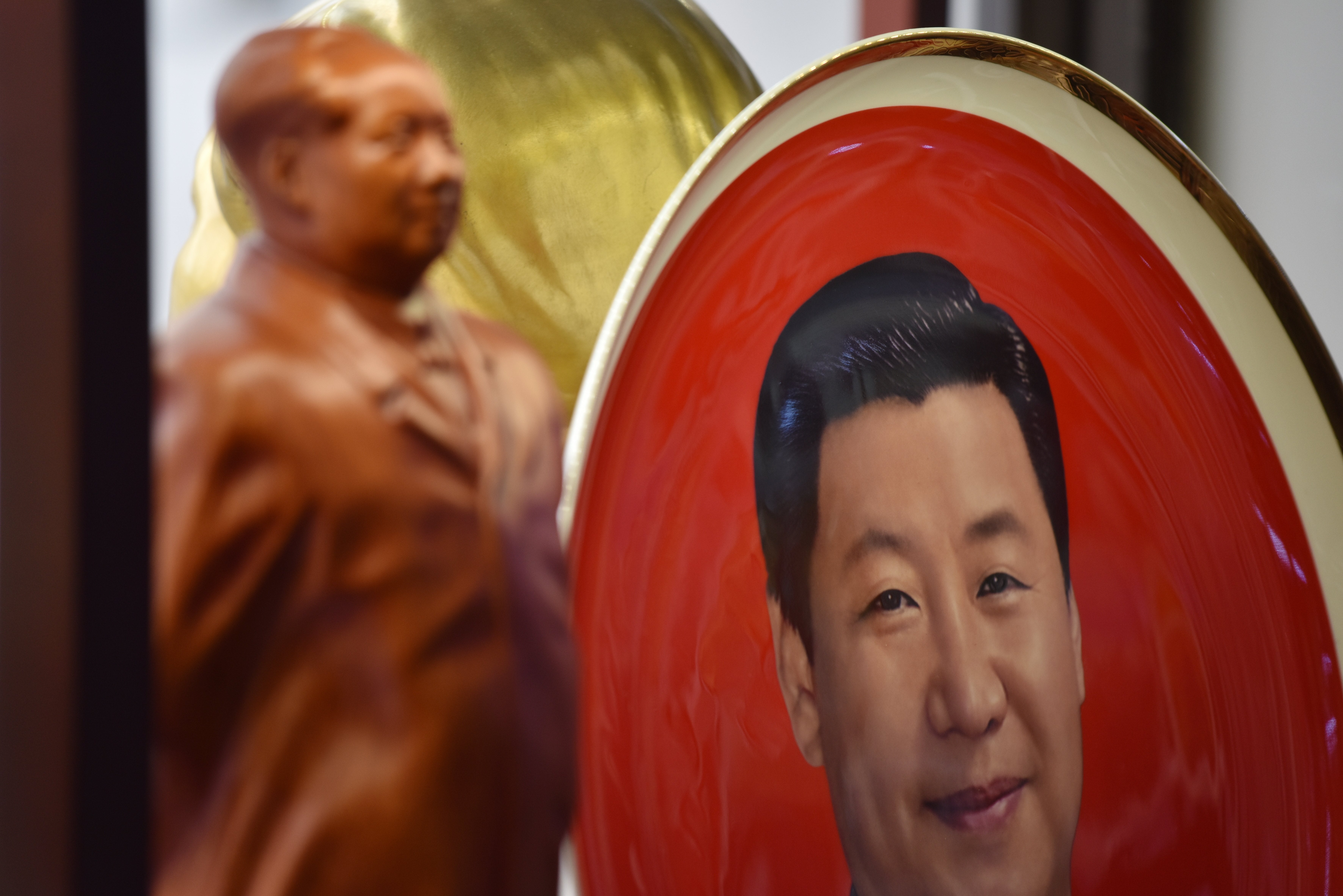 <p>A decorative plate featuring an image of Chinese President Xi Jinping is seen behind a statue of late communist leader Mao Zedong at a souvenir store next to Tiananmen Square in Beijing on 27 February, 2018</p>