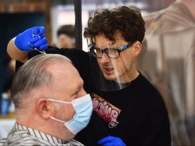 A man wearing a mask has his hair cut at The Men’s Den Barber Shop in Leek, England