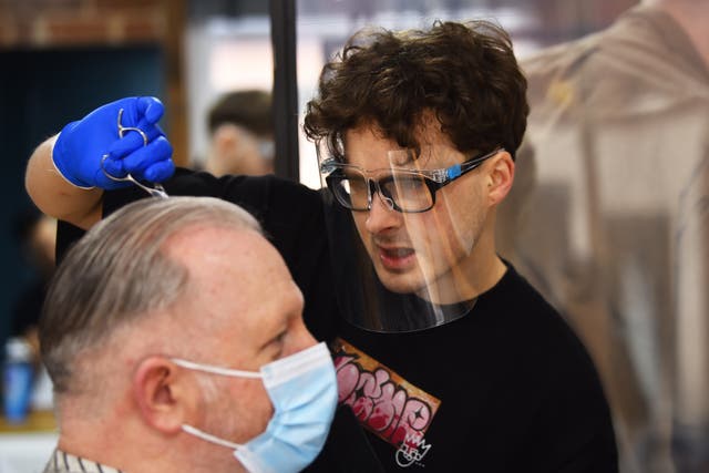A man wearing a mask has his hair cut at The Men’s Den Barber Shop in Leek, England