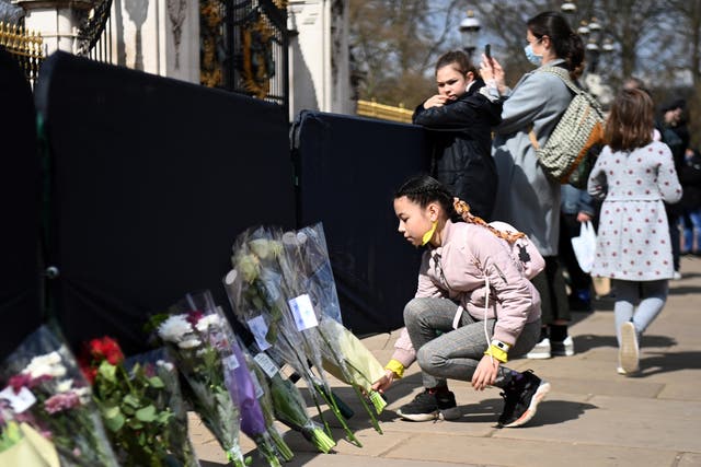 A young girl lays flowers in tribute to Prince Philip outside Buckingham Palace
